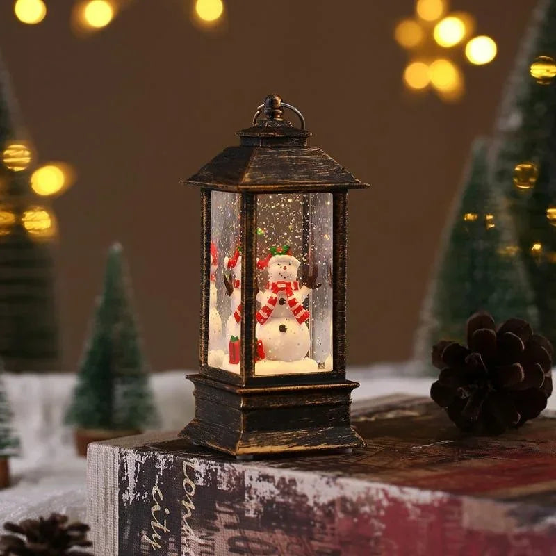 A small black lantern-style Christmas snow globe sits on a rustic surface, with a snowman figure inside and warm blurred holiday lights and trees in the background.