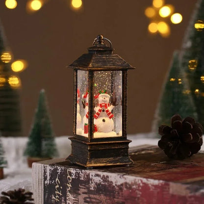 A small black lantern-style Christmas snow globe sits on a rustic surface, with a snowman figure inside and warm blurred holiday lights and trees in the background.
