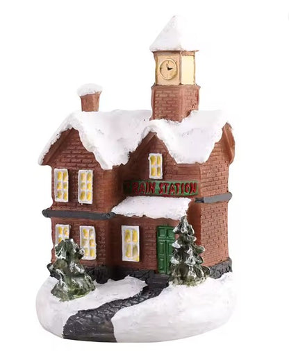 A small decorative village-style house figurine with a snow-covered roof, clock tower, green door, and trees on a white background.