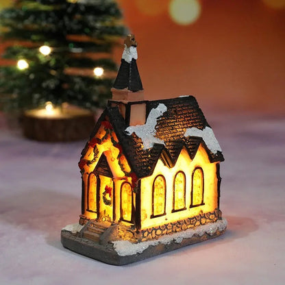 Decorative LED house with a warm glow, placed on a snowy surface with a blurred Christmas tree in the background.