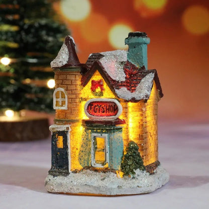 Decorative toy shop house with glowing interior, snow on roof, and 'Toy Shop' sign, against a blurred Christmas tree background.