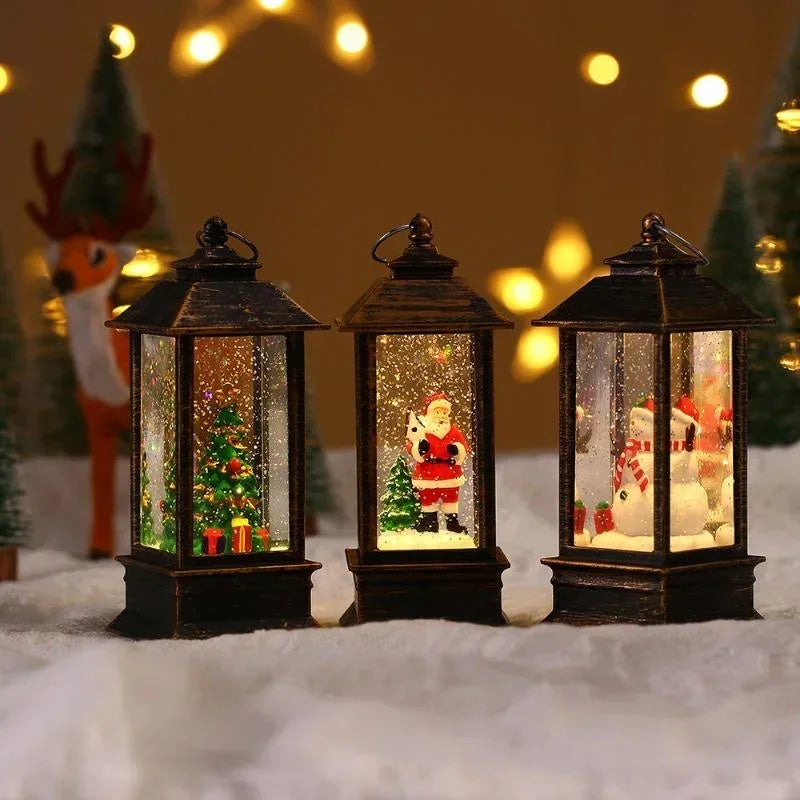 Three lit Christmas snow globe lanterns with dark metal frames, displayed on a white faux-snow surface with warm blurred holiday lights and a small reindeer figure in the background.
